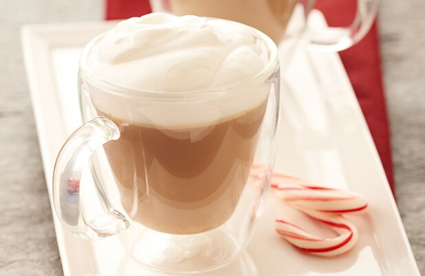 Un moca espumoso de menta en un vaso alto con crema batida y un bastón de caramelo.